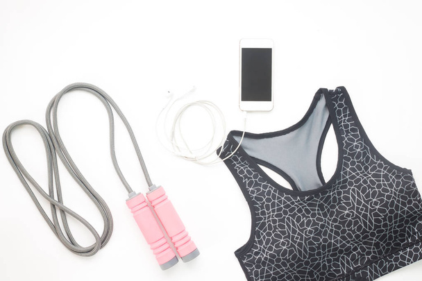Flat lay of smartphone, sport bra and sport equipments on white  - Photo, Image