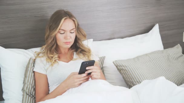 Gadgets in bed: a girl uses a mobile phone in the early morning - Footage, Video