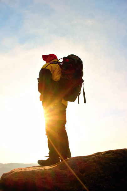 Σιλουέτα του τουρίστας με κόκκινο καπάκι. Πεζοπόρος με μεγάλο σακίδιο στέκονται πάνω σε βράχο. Ηλιόλουστη άνοιξη Χαραυγή - Φωτογραφία, εικόνα