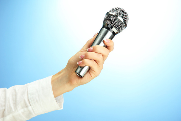 female hand with microphone, on blue background - Zdjęcie, obraz