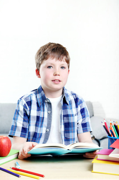 Young boy sitting at the desk and reading book - Foto, afbeelding