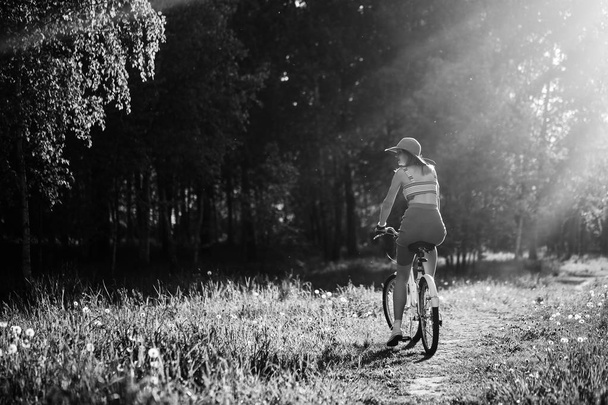 Chica divertida conduciendo bicicleta al aire libre. Concepto de estilo de vida soleado. Mujer vestida y gorra en Campo con dientes de león. Paseo femenino en el parque. Efecto de luz para texto. Copyspace para el diseño. Foto de BW
. - Foto, imagen