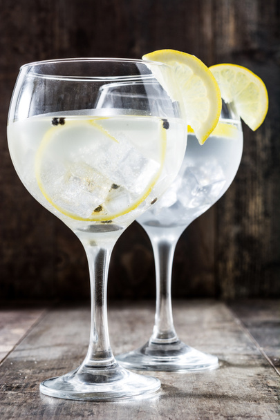Glas gin tonic met citroen op houten achtergrond - Foto, afbeelding