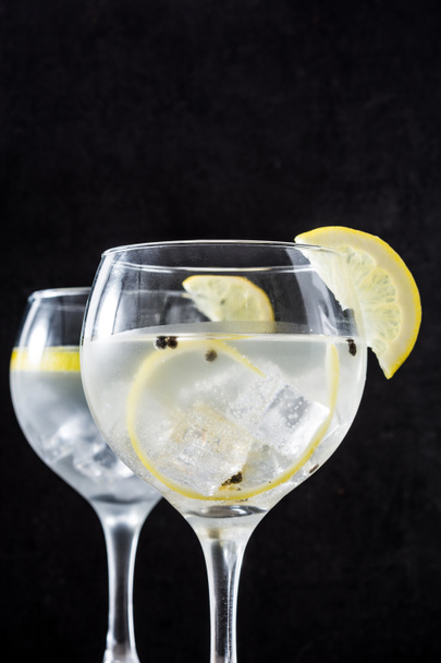 Glass of gin tonic with lemon on black stone background - 写真・画像