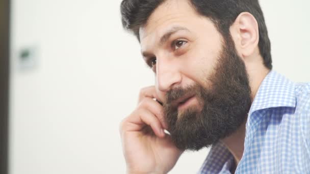 A stylish man with a beard in a bright room speaks on the phone. - Filmagem, Vídeo