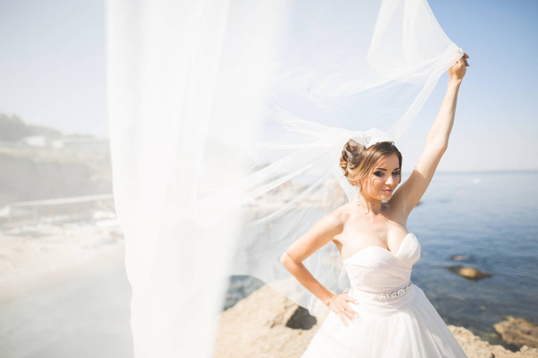schöne junge Braut mit Brautstrauß posiert auf dem Hintergrund Meer - Foto, Bild