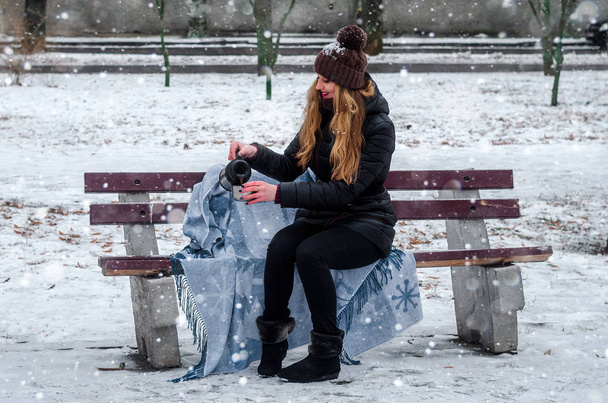 girl sitting on the bench pours himself a thermos of hot drink - Fotó, kép