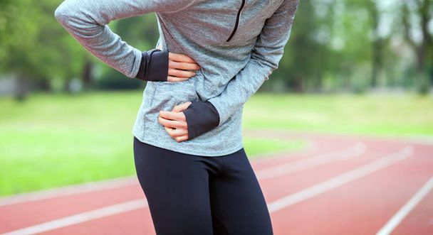 Woman on running track has side cramps during workout - Foto, immagini