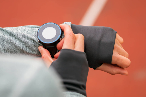 Athletic woman on running track setting up her smart watch fitness accessories - Foto, afbeelding