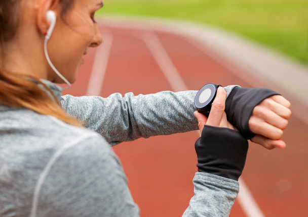 Athletic woman on running track setting up her smart watch fitness accessories - Foto, Imagen