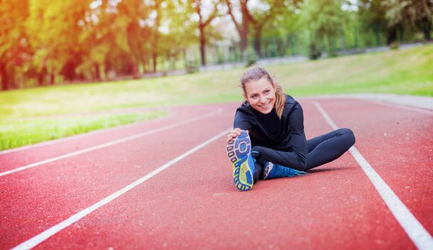 athletische Frau, die sich vor dem Training auf der Laufbahn dehnt, gesunder Lebensstil - Foto, Bild