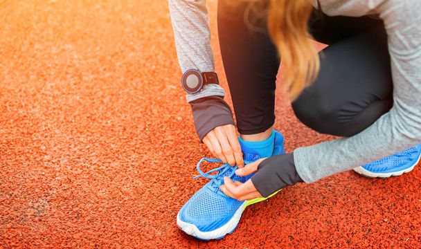 Athletic woman with smart watch on running track tying shoe laces - Valokuva, kuva