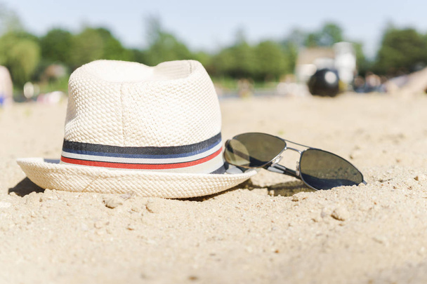 Hat and sunglasses on sand at the sity lake background. - Photo, Image