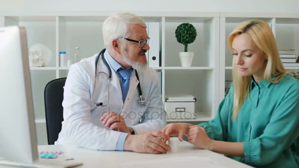 Médico varón de mediana edad caucásico en gafas, hablando de drogas y dando medicamentos a una paciente joven, sentado en el consultorio médico
. - Metraje, vídeo
