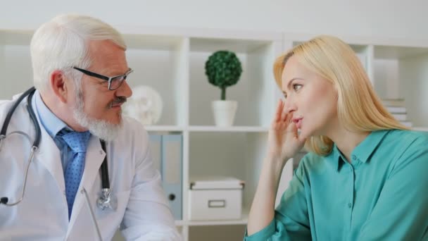 Caucasian midle aged male doctor in glasses with beard listening young female patient telling him that her hurting. Indoor. - Imágenes, Vídeo