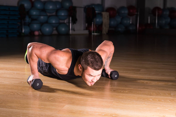 Gym man push-up strength pushup exercise with dumbbell in a fitness workout - Foto, immagini