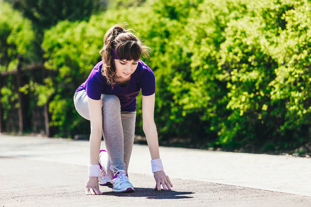 La mujer comienza a correr. Una joven en ropa deportiva se prepara para correr en la naturaleza después de tomar un comienzo bajo
 - Foto, Imagen
