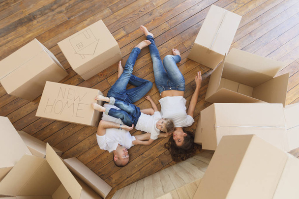Family plays in their new apartment. View from the top on young family moving in new house and unpacking boxes - 写真・画像