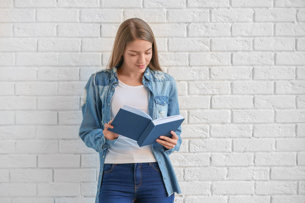 Beautiful young woman with book standing near brick wall - Photo, Image