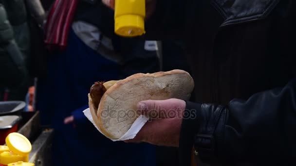 Großaufnahme eines Mannes, der Mayonnaise, Senf auf Wurst in ein Brötchen legt - Filmmaterial, Video