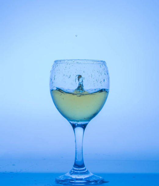 glass with drops of white wine on blue background. - Zdjęcie, obraz