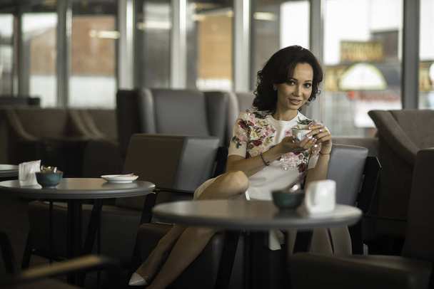 Piękne ciemne włosy kobieta siedzi w restauracji. Patrząc od picia kawy - Zdjęcie, obraz