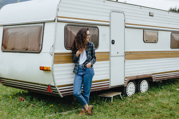 Beautiful girl standing near trailer traveling. Woman in glasses traveling by car. Traveler. - Фото, изображение