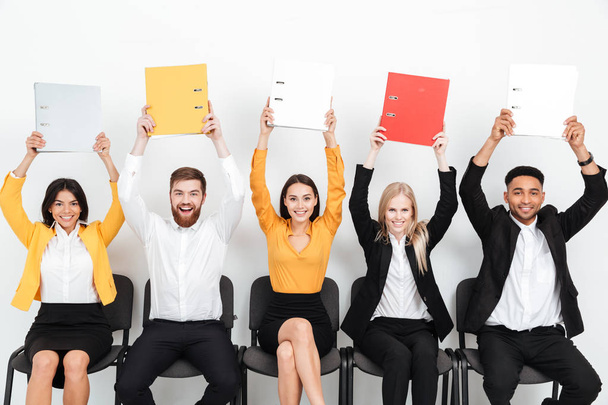 Cheerful colleagues sitting in office holding folders. - Foto, imagen