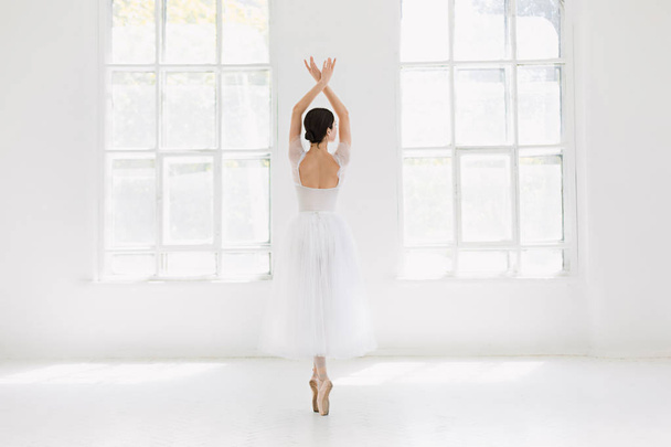 Young and incredibly beautiful ballerina is posing and dancing in a white studio - Фото, изображение