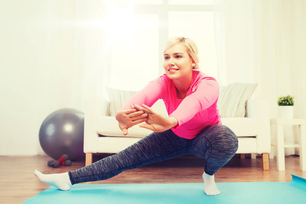 happy woman stretching leg on mat at home - Zdjęcie, obraz