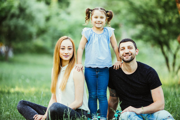 Happy mother, father and daughter playing in the park. Beauty nature scene with family outdoor lifestyle. Happy family resting together on the grass, having fun. Happiness and harmony in family life. - Photo, Image