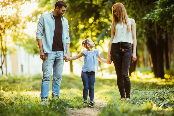 мати, батько і маленька дівчинка гуляють в літньому парку і розважаються
 - Фото, зображення