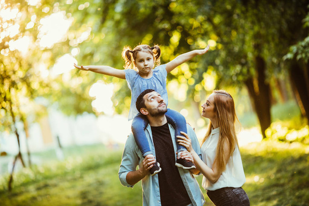 Familia feliz jugando en la naturaleza al final de la tarde la luz del sol en el otoño, verano. Madre, padre e hija jugando en la hierba en el parque, riendo y sonriendo, diversión, alegría
. - Foto, Imagen