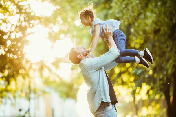 Батько і його дочка грають і обіймаються на відкритому повітрі в літньому парку на заході сонця
. - Фото, зображення
