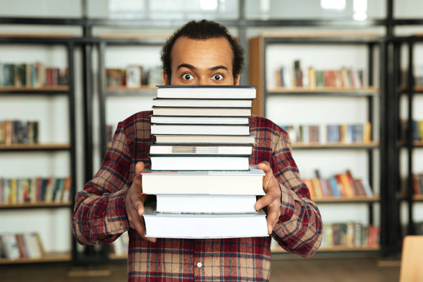Shocked african man student standing in library with books - Фото, изображение