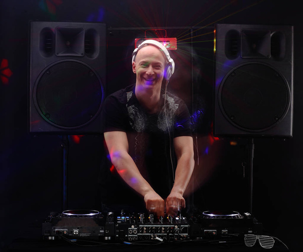Club-DJ mit weißen Kopfhörern, die auf Plattentellern an der Partylinse Musik abspielen. Lautsprecher und Laser im Hintergrund. Langsame Sync-Flash-Technik - Foto, Bild