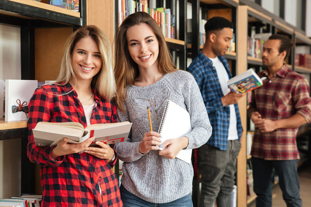 Happy women students standing in library reading books. - Fotó, kép