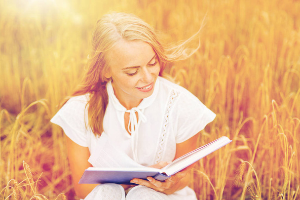 smiling young woman reading book on cereal field - Fotó, kép