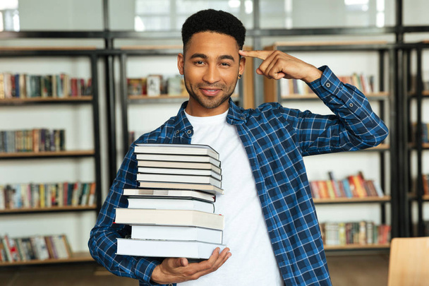 Confident young african male student holding stack of books - Fotografie, Obrázek