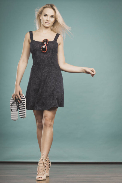 Woman wearing short dress holding flip flops and sunglasses - Fotoğraf, Görsel