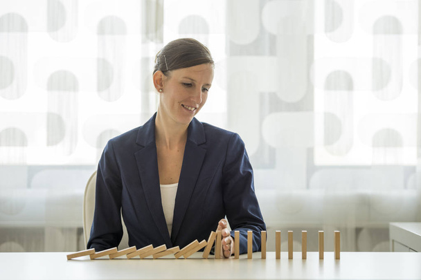 Businesswoman preventing dominoes from crumbling - Foto, Imagen
