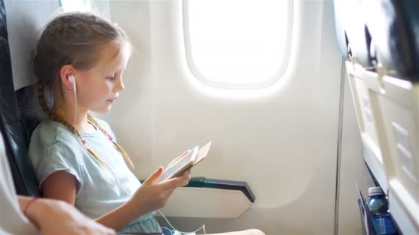 Aranyos kis lány utazik repülőgépen. Aranyos gyerek laptop közelében a repülőgépen ablak - Felvétel, videó