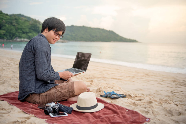 Joven hombre asiático trabajando con el ordenador portátil en la playa
 - Foto, imagen