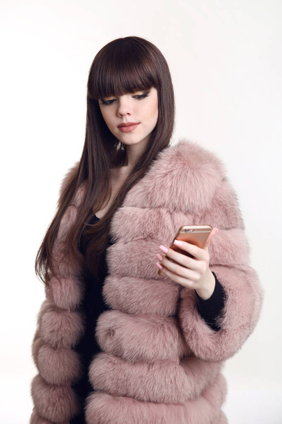 Fashionable brunette girl in pink fur coat holding mobile phone  - Foto, Imagen