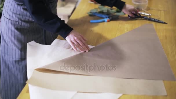 Woman florist folding and cutting paper on desk to wrap flowers - Footage, Video