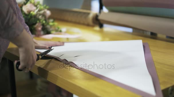 Kwiaciarnia s ręce na jej stole do cięcia papier pakowy - Materiał filmowy, wideo
