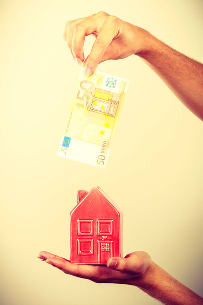 Man putting money into house piggybank - Φωτογραφία, εικόνα