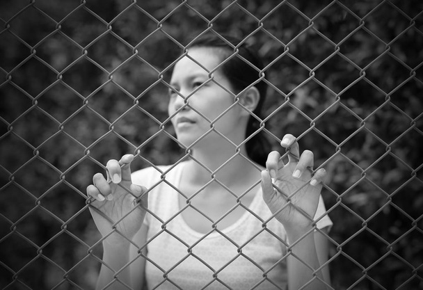 asiatische Frau im Freien schaut mit der Hand heraus, die das Stahlnetz hält, konzentriert sich auf ihre Hände, Schwarz-Weiß-Ton - Foto, Bild