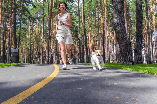 Fitness nainen juoksee ulkona valkoisen koiran kanssa aamulla
 - Valokuva, kuva