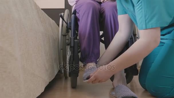 Female caregiver helping senior woman to put her shoes - Filmagem, Vídeo
